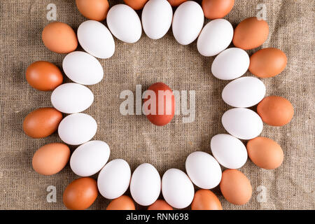 White and brown eggs are lying in circle with one red egg in center on canvas. Stock Photo
