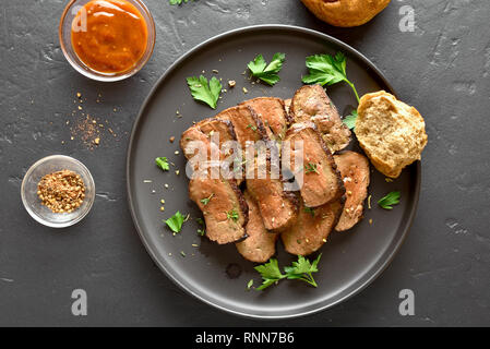 Beef liver on plate over black stone background. Sliced grilled liver(offal) from beef meat. Top view, flat lay Stock Photo