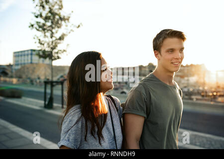 Young couple laughing while walking together along a sidewalk in the city in the late afternoon Stock Photo