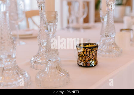 Thin glass candlesticks with white candles. Candles on a holiday table at restaurant Stock Photo