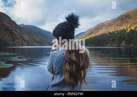 Women with long brown hair and black hat standing at the Upper Lake in Glendalough Ireland