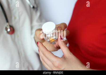 Doctor giving bottle of pills to woman patient in red dress. Concept of medical exam, dose of drugs, vitamins, medical prescription, pharmacy Stock Photo