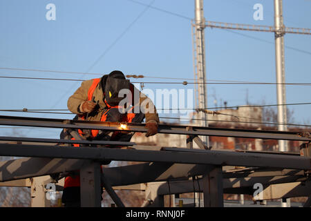 Welder working on scaffolding in the city. Construction worker against the clear blue sky background, welding works Stock Photo