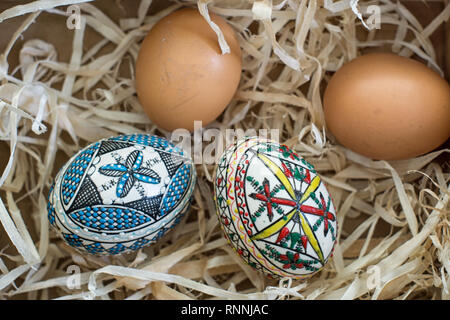 Two decorated easter eggs and two fresh organic eggs on straw Stock Photo