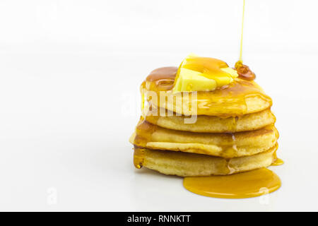 A stack of golden crumpets with butter and syrup drizzled over, set on a white background Stock Photo