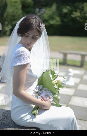 A young pensive couple have a traditional English White Wedding, they are both dark haired and good looking but seem unhappy Stock Photo