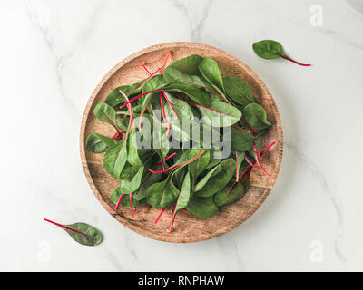 Fresh salad of green chard leaves or mangold on white marble background. Flat lay or top view fresh baby beet leaves on wooden plate. Copy space for t Stock Photo