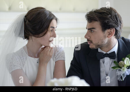 A young pensive couple have a traditional English White Wedding, they are both dark haired and good looking but seem unhappy Stock Photo