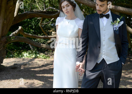 A young pensive couple have a traditional English White Wedding, they are both dark haired and good looking but seem unhappy Stock Photo