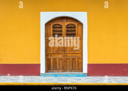 Facade of a house with wooden door and yellow wall in the historic city center of Granada, Nicaragua. Stock Photo