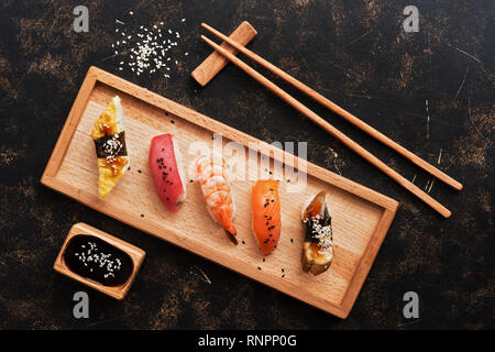 Assorted sushi set on a dark rustic background. Japanese food sushi on a wooden plate, soy sauce, chopsticks. Top view. Sushi Unagi, Syake, Maguro, Eb