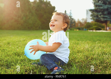 Little boy with a balloon plays, smiles on the grass in the park.  Stock Photo