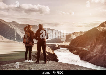 Couple of travelers stands on viewpoint and looks at mountains and river from viewpoint. Travel concept with space for text