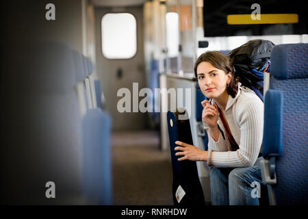 Young woman holding a violin case while sitting  in a train. Stock Photo