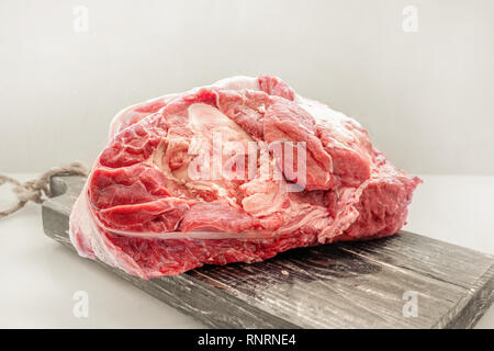 The freshest beef knuckle with bone lies on a wooden thick board on a light background. Close-up. Copy space. Stock Photo