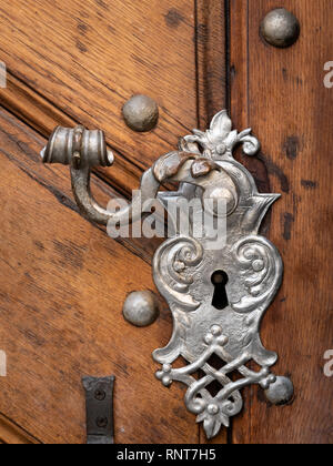 Closeup of a beautiful old doorhandle and decoration made of silver on a brown door Stock Photo
