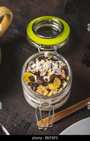 Vertical photo with top view on white yogurt. Yogurt is in small glass jar with metal lock and sealed cover. Muesli with dried food is layered in and  Stock Photo