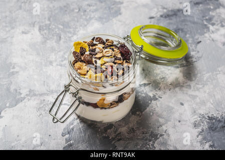 Horizontal photo of white yogurt. Yogurt is in small glass jar with metal lock and sealed cover. Muesli with dried food is layered in and on yogurt. G Stock Photo