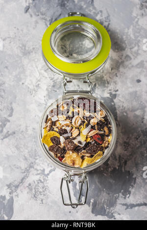 Vertical photo with top view on white yogurt. Yogurt is in small glass jar with metal lock and sealed cover. Muesli with dried food is layered in and  Stock Photo