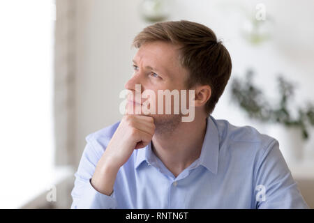 Thoughtful businessman sitting at workplace looking away Stock Photo