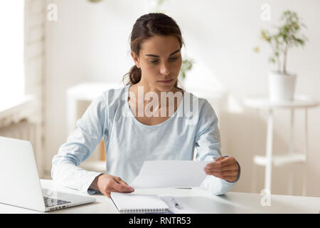 Serious woman sitting at desk reading letter Stock Photo