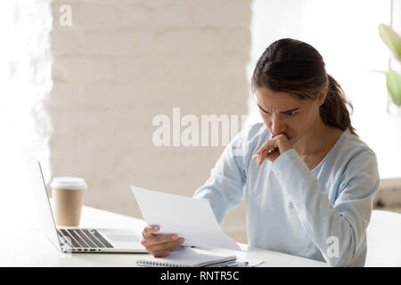 Frustrated young woman sitting at table reading letter Stock Photo