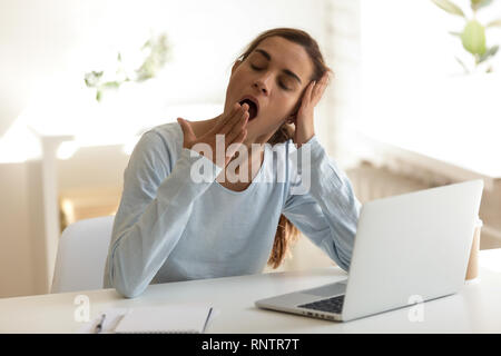 Bored female sitting at workplace feels sleepy putting head in her hand  Stock Photo