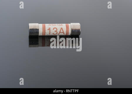 Domestic appliance electrical 13 Amp fuse (Ceramic Cartridge type) on reflective black background. Metaphor electrical safety. 25mm L x 6.3mm D Stock Photo