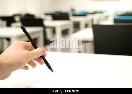 Classroom empty. High school or university student holding pen writing on paper answer sheet. Exam test room Stock Photo
