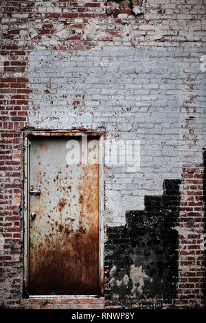 Old rusty metal or steel door in a weathered brick wall suitable for a rustic background. Stock Photo