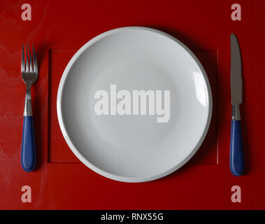 an empty white plate with fork and knife - red background - closeup Stock Photo