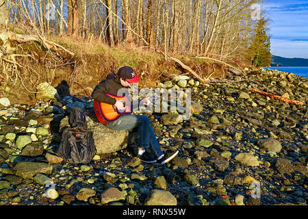 Young man playing guitar on rocky beach Stock Photo
