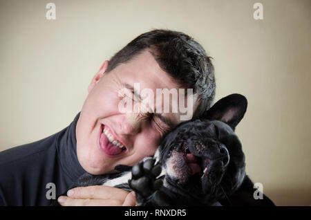 portrait of smiling, happy man. male person hugs black, active, French bulldog. handsome fool around with pet. cheerful guy in delight have fun. satisfied, delighted human hold pleased, young dog Stock Photo