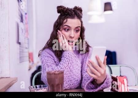Surprised young woman in violet sweater being shocked with information Stock Photo