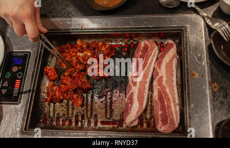 Korean style barbecue with raw pork belly and spicy bulgogi meat on hot stove plate grill. Stock Photo