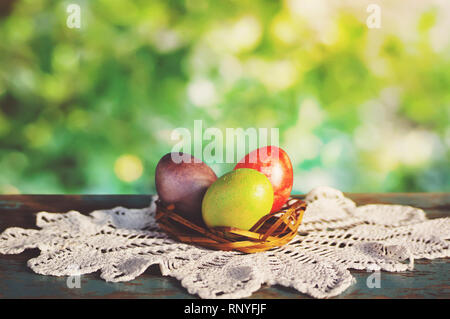 Basket of easter eggs on white rustic table cloths on an old vintage table at sunny day. Breakfast is served for Easter in the green spring garden. Stock Photo