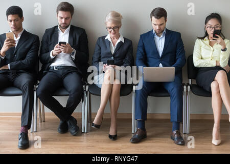 Diverse businesspeople sitting in row using devices phones and laptop Stock Photo