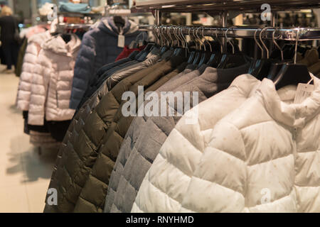 Row of white green and gray down jackets on the rack clothing