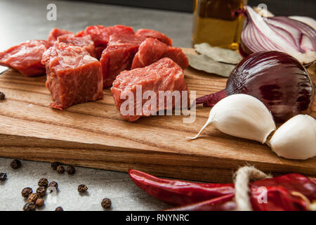 Uncooked fresh diced beef meat with herbs and oil on an old rustic wooden kitchen board over stone background. Stock Photo
