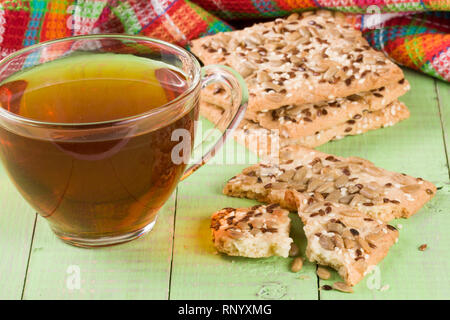 crispy bread with seeds of sunflower, flax and sesame seeds with a cup of tea on a green wooden background. Stock Photo
