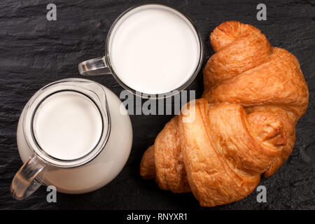 A jug and a glass of milk with two croissants on a black stone background. Top view. Stock Photo