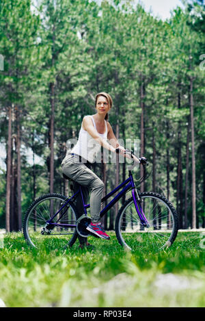 Woman sitting on bicycle in forest Stock Photo