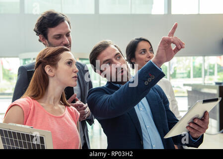 Male architect pointing while talking with his colleagues in hotel lobby Stock Photo