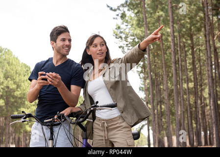 Young couple standing with bicycles in pine forest Stock Photo