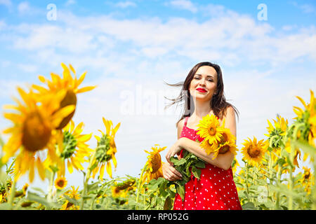Pretty brunette woman wearing red polka dots dress in sunflower field Stock Photo