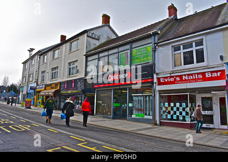 A row of traditional shops in the town centre of Bridgend, S.Wales. Shoppers walking along street with shopping bags. Stock Photo