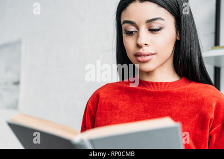 pretty african american girl in red sweatshirt reading book Stock Photo