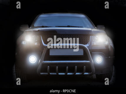 SUV is isolated on a dark background with luminous headlights Stock Photo