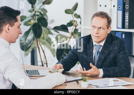 businessman in blue jacket sitting in office and giving to worker with broken arm money in office, compensation concept Stock Photo