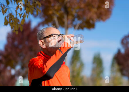 Handsome senior jogging man drinking fresh water from bottle after morning run Stock Photo